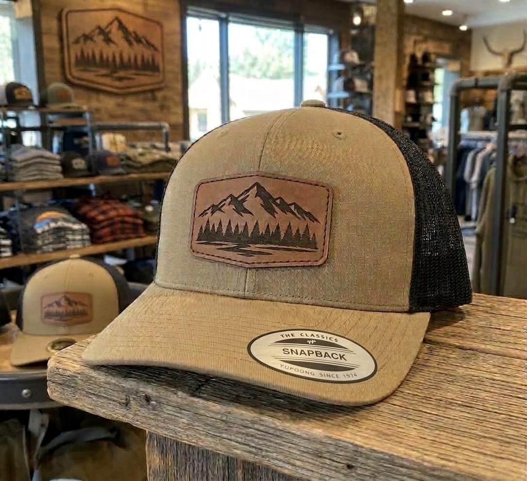 Rendering, actual product may vary slightly: YP Classics 6606 retro trucker hat in Coyote Brown/Black with a sample laser-engraved leatherette patch (your design goes here)