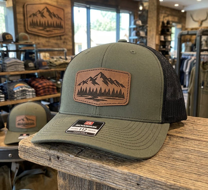 Rendering, actual product may vary slightly: Richardson 112 trucker hat in Loden/Black with a sample laser-engraved leatherette patch (your design goes here)